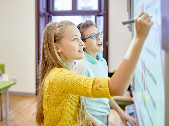 Två skolungdomar står vid en whiteboard-tavla och skriver